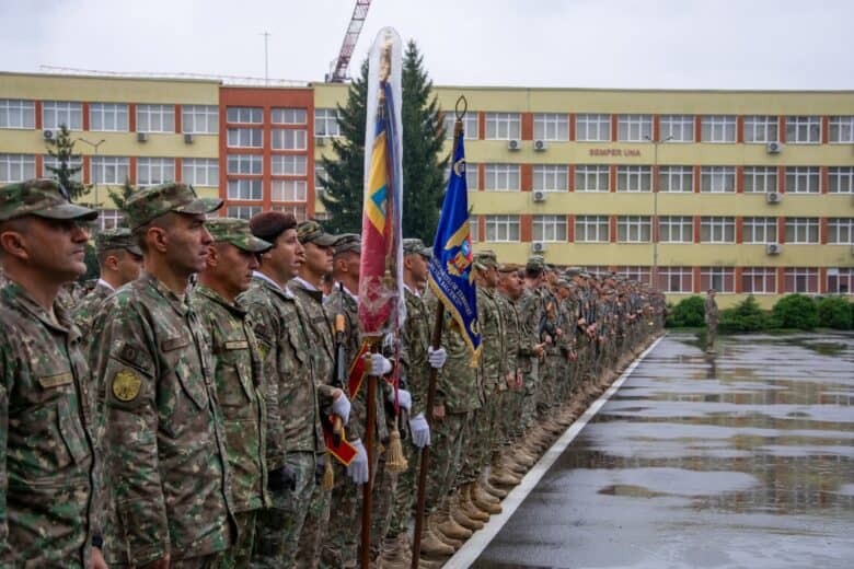 Soldați în uniformă camouflage la ceremonia militară în curtea unei școli din Sibiu, România, cu drapelul național și drapelul militar, într-o zi ploioasă, în centrul orașului, reprezentând patriotism și disciplina.
