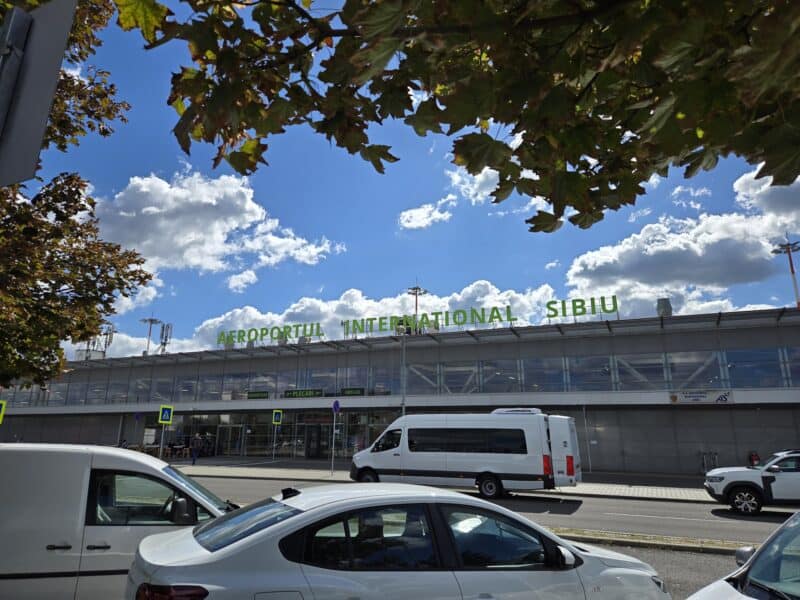 Aeroport Internațional Sibiu vedere din exterior, cu mașini parcate și semnalizare rețea de transport, sub cer senin și aer proaspăt, reprezentând infrastructură modernă pentru transportul aerian în Sibiu.