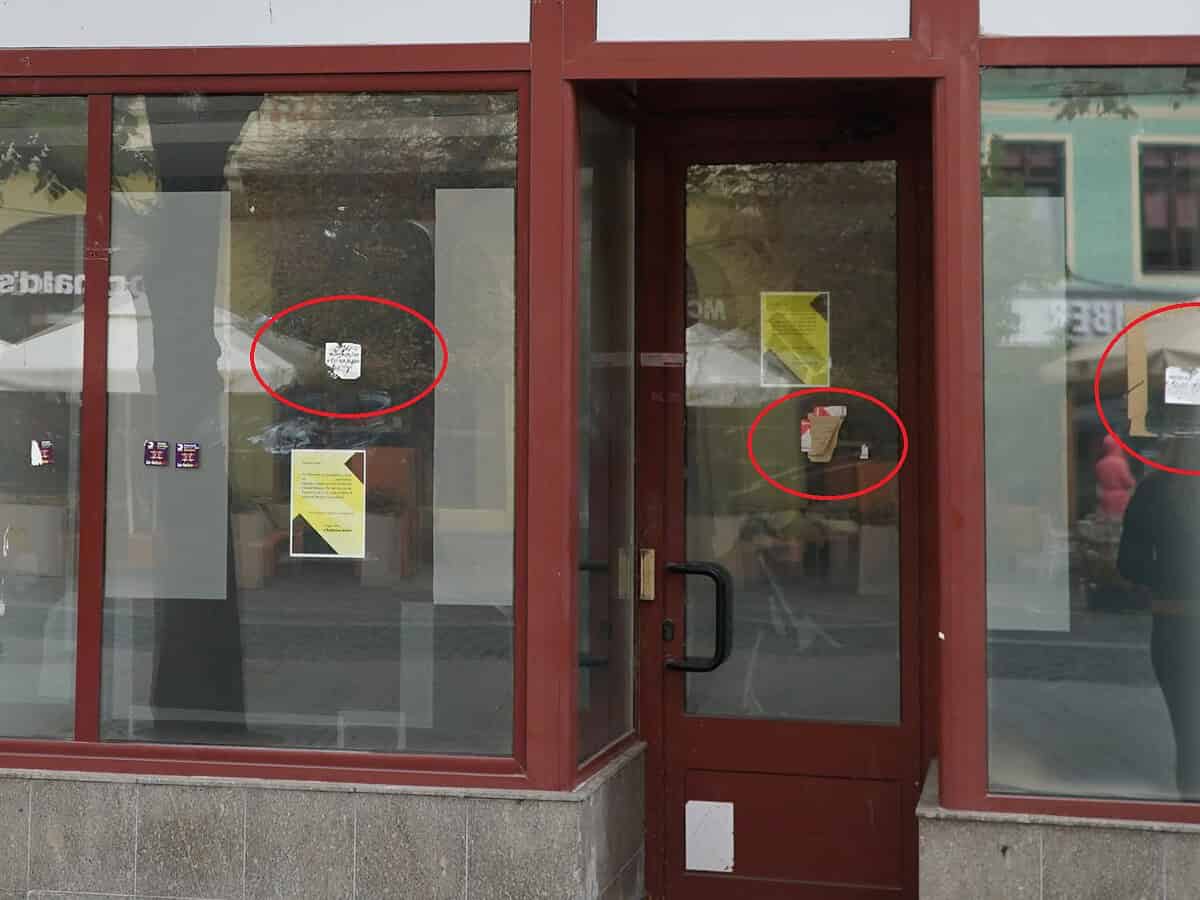 Mici stickere pe geamul unei uși din oraș, apărute ca urmare a unor probleme de întreținere sau vandalism, cu semne și mesaje temporare, în stil urban, reprezentând un aspect frecvent în peisajul citadin.
