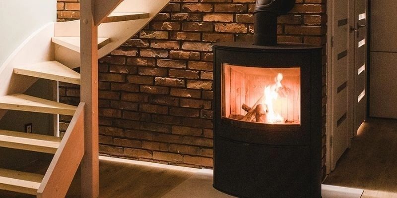 Sobă modernă pe lemne, design compact, amplasată sub o scară din lemn