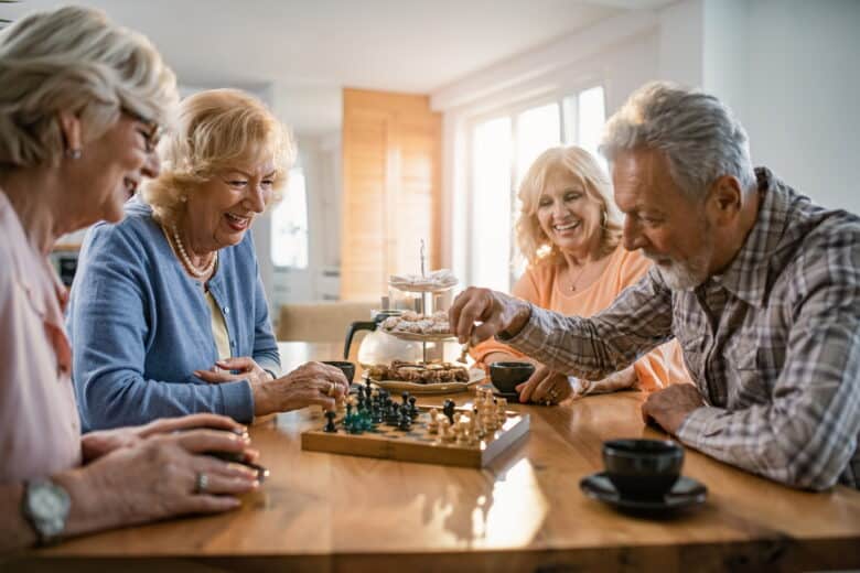 Patru seniori zâmbitori jucând șah la o masă de cafea