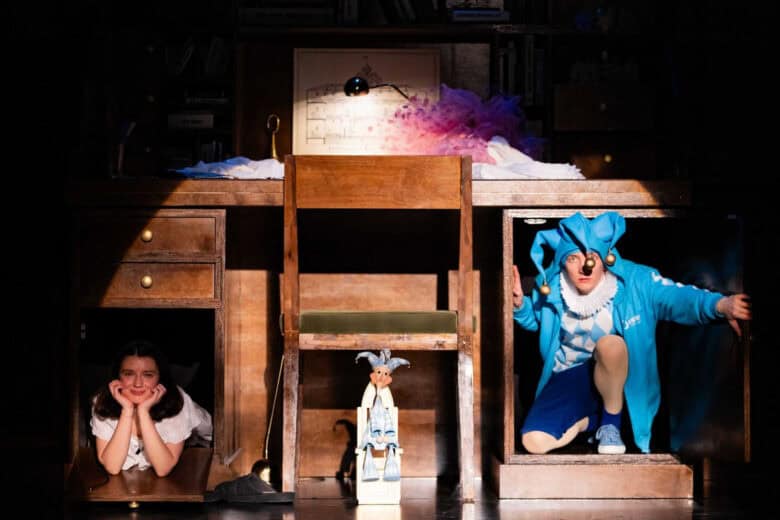 Scenă dintr-un spectacol pentru copii al Teatrului Gong, cu un birou din lemn și un personaj în costum albastru