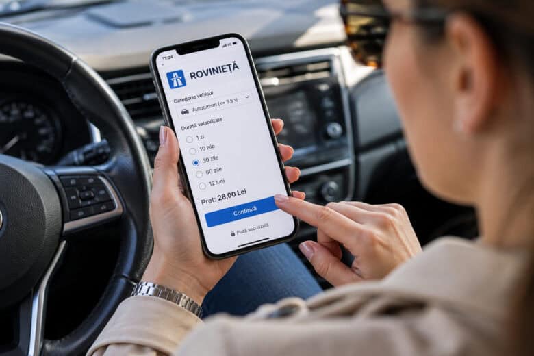 Șoferiță ținând în mână un telefon cu aplicația de plată a rovinietei deschisă
