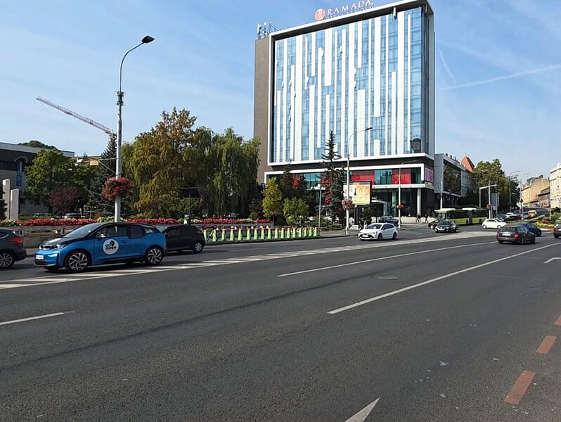 Trafic fluid pe un bulevard din centrul Sibiului, cu un hotel înalt în fundal, într-o zi însorită